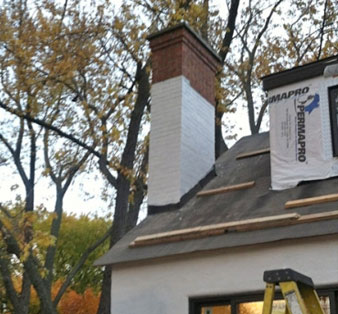 Brick chimney partially painted white, undergoing restoration by Top Hat Masonry Repair